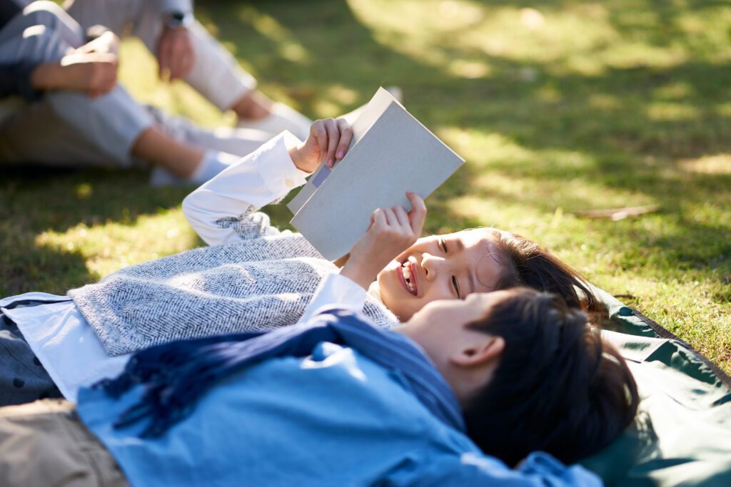 Two kids laying in grass, smiling and reading a book
